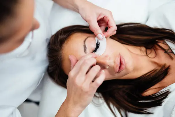 stock image Beautiful young adult woman receiving professional eyelash makeup treatment. Cosmetician is smiling and looking at camera. Beauty and cosmetics business. 