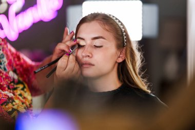 Profesyonel güzellik uzmanı güzel genç bir kadının yüzüne makyaj yapıyor. Muhteşem bir kadın modelle profesyonel makyaj stüdyosu çalışması..