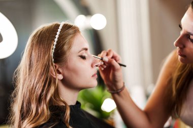 Profesyonel güzellik uzmanı güzel genç bir kadının yüzüne makyaj yapıyor. Muhteşem bir kadın modelle profesyonel makyaj stüdyosu çalışması..