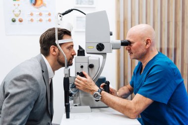 Çekici erkek doktor göz doktoru modern klinikteki yakışıklı orta yaşlı adamın görüşünü kontrol ediyor. Göz hekimliği kliniğinde doktor ve hasta kontrolü sırasında.. 