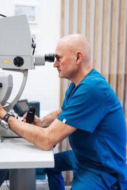 Görme kontrolü sırasında yüksek teknolojili tıbbi cihaz kullanan deneyimli bir kıdemli doktor. Göz hastalıklarının teşhisi ve tedavisi için modern bir klinik. Sağlık ve Tıp Konsepti.