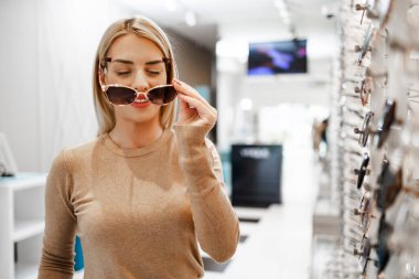Modern optik mağazada gözlük çerçevesi seçen güzel ve şık bir kadın.. 