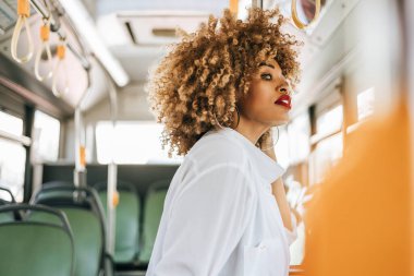 Şehir otobüsünde duran güzel ve şık siyahi kadın. O mutlu ve gülümsedi. Modern şehir yaşam tarzı kavramı. Parlak güneşli bir gün.