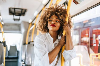 Şehir otobüsünde duran güzel ve şık siyahi kadın. O mutlu ve gülümsedi. Modern şehir yaşam tarzı kavramı. Parlak güneşli bir gün.