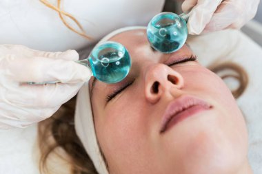 Dondurma çubukları ya da buz küreleriyle kriyoterapide eğlenen güzel genç bir kadın. Kızarıklığı, iltihaplanmayı ve deri şişkinliğini azaltmak için modern ve popüler güzellik prosedürü. Cilt tedavisi kavramı.