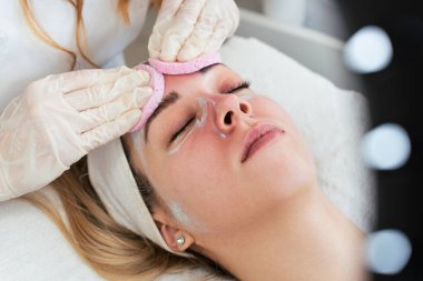 Güzel ve çekici genç bir kadın bitkisel kil maskeyle profesyonel güzellik ya da cilt bakımı görüyor. Modern ve popüler yüz bakımı kavramı. Spa salonu. Yüksek açı görünümü.