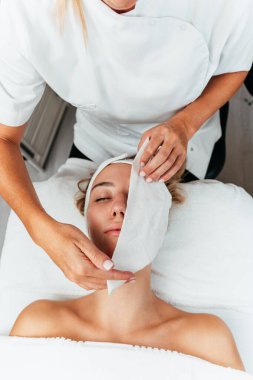 Güzel, rahat, genç bir kadın gözleri kapalı uzanmış bir kaplıca salonunda yüz masajının keyfini çıkarıyor. Bayan müşteri cilt bakımı tedavisinden zevk alıyor. Sağlık ve güzellik kavramı.