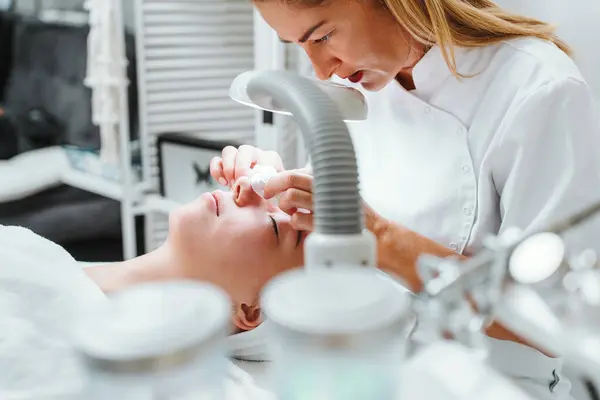 stock image Professional beautician manually removing acne and pimples from young woman's face in a modern equipped beauty spa studio. Beautification and skin health concept.