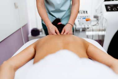 Beautiful young adult brunette receiving professional relaxation massage treatment at beauty spa salon.