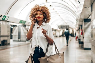 Güzel, modaya uygun siyah kadın metro istasyonunda duruyor. O mutlu ve akıllı telefonundan biriyle konuşuyor. Toplu taşıma ve kentsel yaşam konsepti.