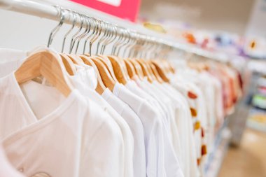 Beautiful baby clothes hanging arranged on rack in a modern store or shop. Shopping interior concept. No people.