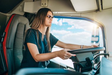 Genç ve güzel bir kadının portresi. Profesyonel kamyon şoförü oturuyor ve büyük bir kamyon sürüyor. Aracın içinde. İnsanlar ve ulaşım kavramı.
