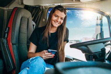 Büyük bir kamyonda oturan, kameraya bakıp gülümseyen güzel, genç kadın kamyon şoförünün portresi. Aracın içinde. İnsanlar ve ulaşım kavramı.