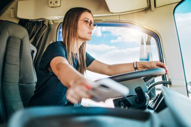 Genç ve güzel bir kadının portresi. Profesyonel kamyon şoförü oturuyor ve büyük bir kamyon sürüyor. Araba kullanırken tehlikeli bir şekilde akıllı telefon almaya çalışıyor..