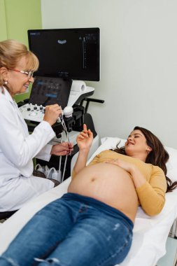 Female doctor doing ultrasound scan for a beautiful pregnant woman. Side view. Modern pregnancy and healthcare concept.
