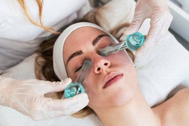 Dondurma çubukları ya da buz küreleriyle kriyoterapide eğlenen güzel genç bir kadın. Kızarıklığı, iltihaplanmayı ve deri şişkinliğini azaltmak için modern ve popüler güzellik prosedürü. Cilt tedavisi kavramı.