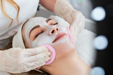 Güzel ve çekici genç bir kadın bitkisel kil maskeyle profesyonel güzellik ya da cilt bakımı görüyor. Modern ve popüler yüz bakımı kavramı. Spa salonu. Yüksek açı görünümü.