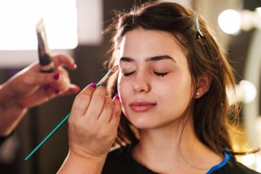 Profesyonel güzellik uzmanı güzel genç bir kadının yüzüne makyaj yapıyor. Muhteşem bir kadın modelle profesyonel makyaj stüdyosu çalışması..