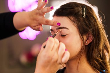 Profesyonel güzellik uzmanı güzel genç bir kadının yüzüne makyaj yapıyor. Muhteşem bir kadın modelle profesyonel makyaj stüdyosu çalışması..