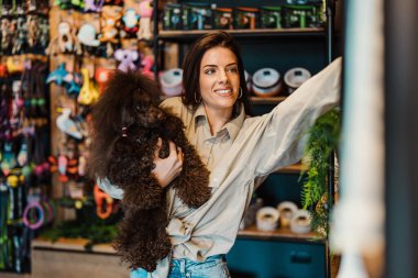 Güzel genç bir kadın, sevimli kahverengi oyuncak kanişiyle modern evcil hayvan dükkanında eğleniyor.. 