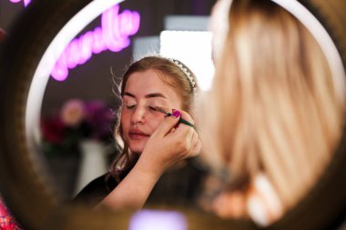 Profesyonel güzellik uzmanı güzel genç bir kadının yüzüne makyaj yapıyor. Muhteşem bir kadın modelle profesyonel makyaj stüdyosu çalışması..