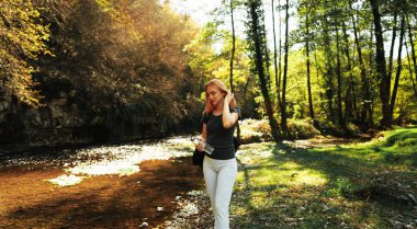 Güzel kızıl saçlı kadın ormanda yürüyor ve bir şişe içme suyuyla koşuyor. Doğa konseptinde sağlıklı yaşam tarzı ve spor.