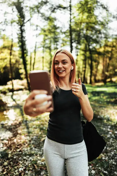 Güzel kızıl saçlı sporcu kadın ormanda koşuyor ve yürüyor. Müzik dinlemek ve arkadaşlarıyla video görüşmeleri için akıllı telefon ve kablosuz kulaklık kullanıyor.. 