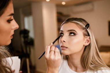 Makyaj süreci. Makyaj için makyaj yapan profesyonel bir sanatçı. Güzellik salonundaki güzel sarışın kadının portresi. Önde gelen güzel yüzük ışığına bak.