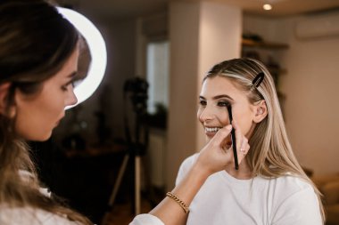 Makyaj süreci. Makyaj için makyaj yapan profesyonel bir sanatçı. Güzellik salonundaki güzel sarışın kadının portresi. Önde gelen güzel yüzük ışığına bak.