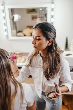Makyaj süreci. Makyaj için makyaj yapan profesyonel bir sanatçı. Güzellik salonundaki güzel sarışın kadının portresi. Önde gelen güzel yüzük ışığına bak.