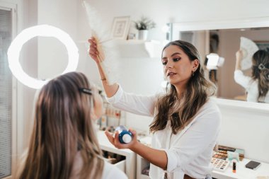 Makyaj süreci. Makyaj için makyaj yapan profesyonel bir sanatçı. Güzellik salonundaki güzel sarışın kadının portresi. Önde gelen güzel yüzük ışığına bak.
