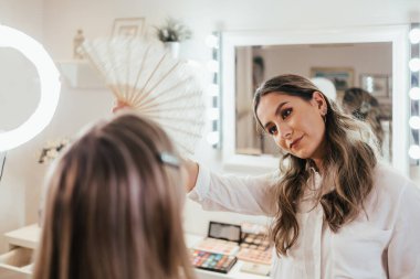 Makyaj süreci. Makyaj için makyaj yapan profesyonel bir sanatçı. Güzellik salonundaki güzel sarışın kadının portresi. Önde gelen güzel yüzük ışığına bak.