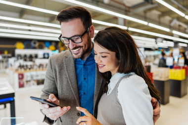 Beautiful and happy middle age couple buying consumer tech products in modern home appliances store. They are choosing smart phone or digital tablet. People and consumerism concept.
