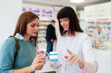 Güzel kadın eczacı müşteriyle konuşur ve doğru ilaçları seçmesine yardım eder. Eczane işi ve çalışanlar.