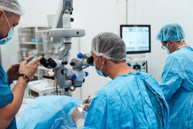 Yetenekli cerrah ve tıbbi ekibi yaşlı bir hastaya hassas bir göz ameliyatı yaparak en son tıbbi teknoloji ve ileri teknoloji ile görme yetisini geri kazandırıyor. Modern göz ameliyatı konsepti.