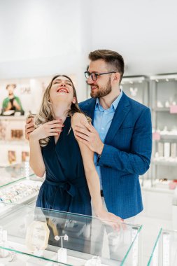 Modern kuyumcuda alışveriş yapan güzel bir çift. Genç bir kadın denesin. Muhteşem, pahalı kolye ve küpeler. Moda tarzı ve tüketim konsepti.