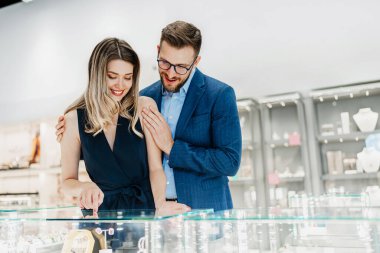 Modern kuyumcuda alışveriş yapan güzel bir çift. Genç bir kadın denesin. Muhteşem, pahalı kolye ve küpeler. Moda tarzı ve tüketim konsepti.