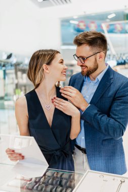 Modern kuyumcuda alışveriş yapan güzel bir çift. Genç bir kadın denesin. Muhteşem, pahalı kolye ve küpeler. Moda tarzı ve tüketim konsepti.