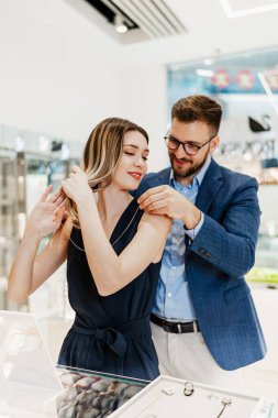 Modern kuyumcuda alışveriş yapan güzel bir çift. Genç bir kadın denesin. Muhteşem, pahalı kolye ve küpeler. Moda tarzı ve tüketim konsepti.