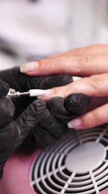 Profesyonel manikürcü ya da kuaför müşteri tırnağına oje sürerken tırnak törpüsü kullanıyor. Yakın çekim. Yüzeyin derinliği. Modern güzellik SPA ve kozmetik konsepti.