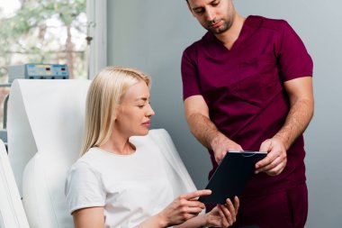 Güzellik kliniğindeki güzel ve mutlu sarışın kadın. Oturup yakışıklı erkek doktorla yüz estetiği hakkında konuşuyor..