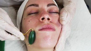 Güzel bir kadın Gua Sha yüz drenajı masajı yaptırıyor. Modern ve popüler invazif olmayan cilt tedavisi kavramı.