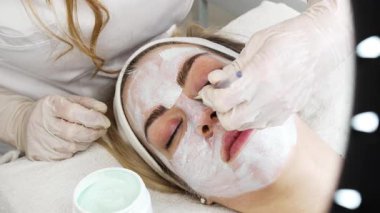 Güzel ve çekici genç bir kadın bitkisel kil maskeyle profesyonel güzellik ya da cilt bakımı görüyor. Modern ve popüler yüz bakımı kavramı. Spa salonu. Yüksek açı görünümü.