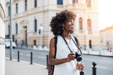 Genç siyah bayan turist güzel bir Avrupa şehrinin sokaklarında yürümekten zevk alıyor. O mutlu ve fotoğraf makinesini fantastik mimari fotoğraflar çekmek için kullanıyor. Parlak güneşli bir gün.