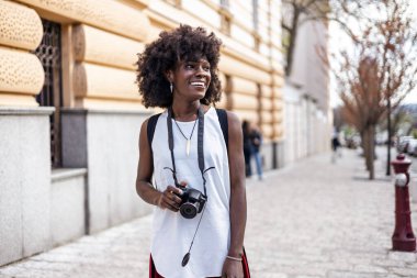Genç siyah bayan turist güzel bir Avrupa şehrinin sokaklarında yürümekten zevk alıyor. O mutlu ve fotoğraf makinesini fantastik mimari fotoğraflar çekmek için kullanıyor. Parlak güneşli bir gün.