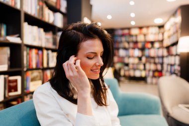 Güzel bayan öğrenci düşünceli bir şekilde kanepede oturuyor ve kütüphanede ya da kitapçıda kitap okuyor. Eğitim kavramı.