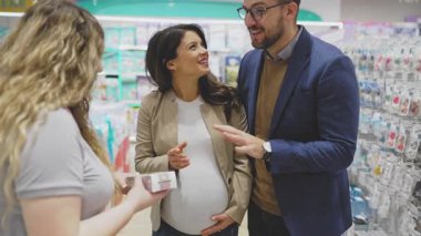 Çekici orta yaşlı çift yeni bebekleri için kıyafet ve alet almaktan zevk alıyor. Yardım etmeye çalışan deneyimli bir satıcı. Bebek konsepti bekleniyor..