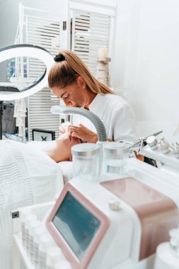 Modern donanımlı güzellik merkezinde profesyonel bir güzellik uzmanı genç bir kadının yüzündeki sivilceleri ve sivilceleri elle temizliyor. Yüz Temizleme. Güzelleştirme ve cilt sağlığı kavramı.