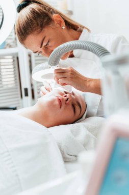Modern donanımlı güzellik merkezinde profesyonel bir güzellik uzmanı genç bir kadının yüzündeki sivilceleri ve sivilceleri elle temizliyor. Yüz Temizleme. Güzelleştirme ve cilt sağlığı kavramı.