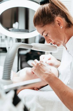 Modern donanımlı güzellik merkezinde profesyonel bir güzellik uzmanı genç bir kadının yüzündeki sivilceleri ve sivilceleri elle temizliyor. Yüz Temizleme. Güzelleştirme ve cilt sağlığı kavramı.